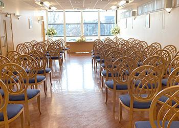 A photo taken at the back of the wedding suite showing a column of chairs on each side and the registrar's desk in front of the window at the other side of the room.