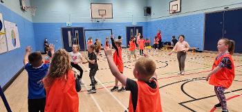 A large group of children playing basketball in an indoor gym hall