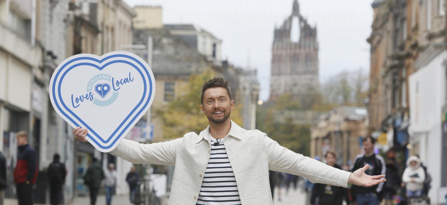 STV weatherman Sean Batty holing up a Scotland Loves Local sign with Paisley High Street blurred in the background