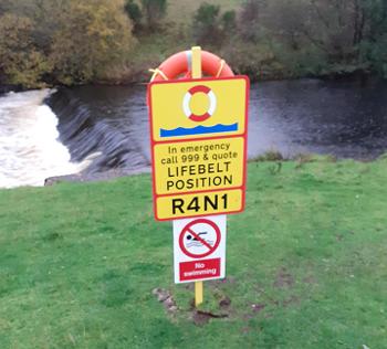 A water safety sign showing the GPS code on the bank beside a viaduct 