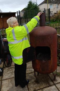 Image of Lesley Rodgers wearing high visibility jacket outdoors reaching to top of furnace