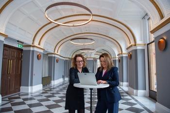 Two women standing at a tall table working on a lap top and smiling