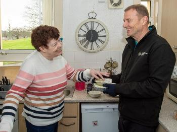 A man and woman smiling as he hands her a tinfoil box with hot food inside