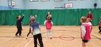 A handful of children play hand ball in a gymhall with Councillor Marie McGurk.