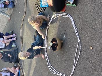 Children toast a marshmallow in a fire pit outside in a playground.