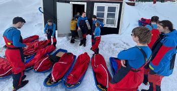 10 pupils prepare their sledges outside a storage house in a snowy field.