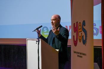 Jackson Katz stands at a podium talking, gesturing outwards with his hands.