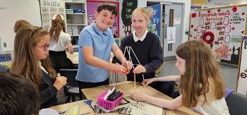 Four pupils work together to create a structure out of straws in a classroom.