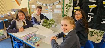 Four pupils smile while working at their desk in a classroom.