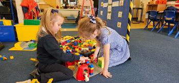 Two young pupils work together to build a structure out of Lego while sitting on the floor.