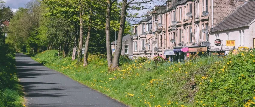 Walking path beside trees and grass with a row of houses behind them in Bridge of Weir.