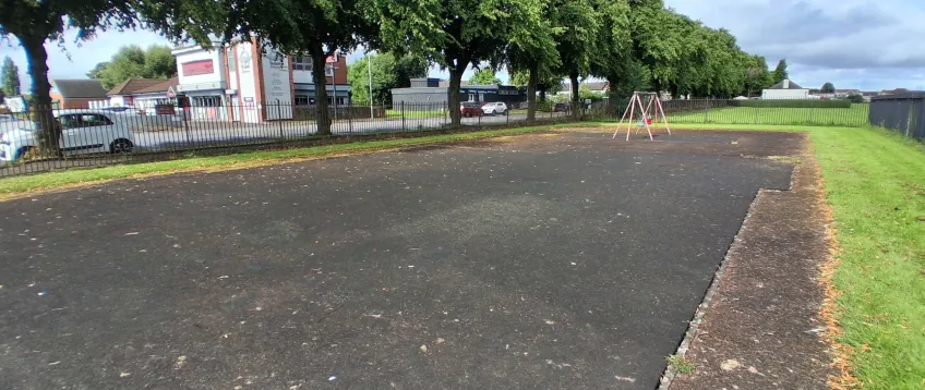 A tarmac area with nothing on it, on the edge of an area of grass.