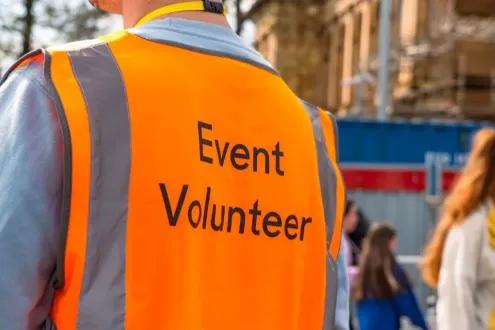 A person wearing an orange hi-vis jacket that says 'Event Volunteer' on the back