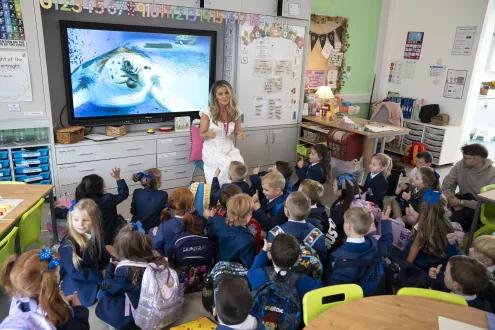 Children sit on their classroom floor and listen to their teacher.