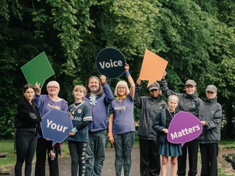 A group of local people of different ages, genders and ethnicities holding up our Voice Matters placards