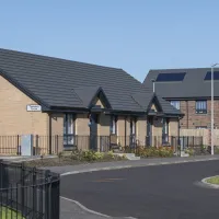 New houses and a new road in front of them, with some plants in front of them and some grass and a newly planted tree.