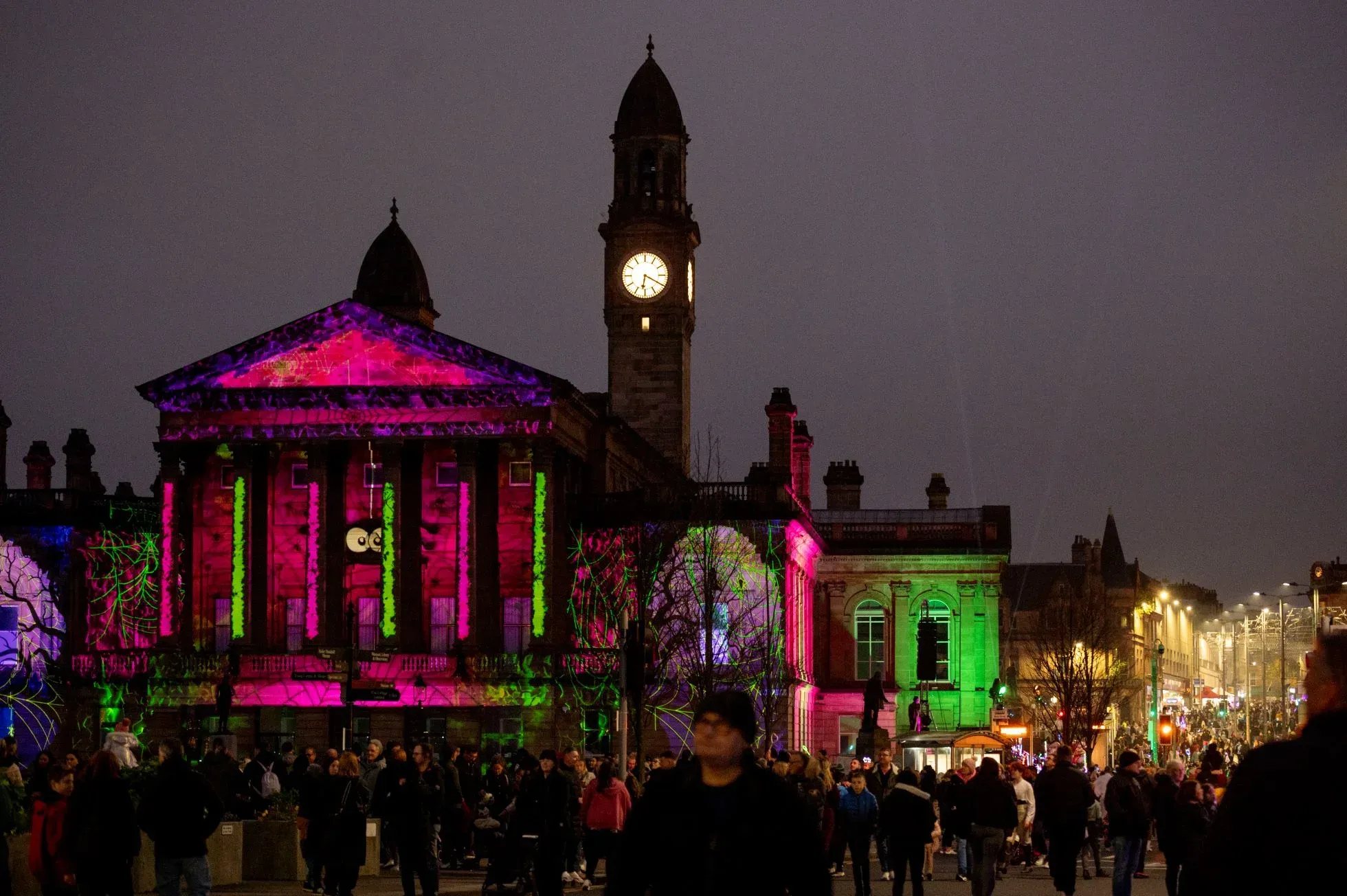 Crowds at Paisley Halloween Parade in front of a lit-up historic building with spooky projections.