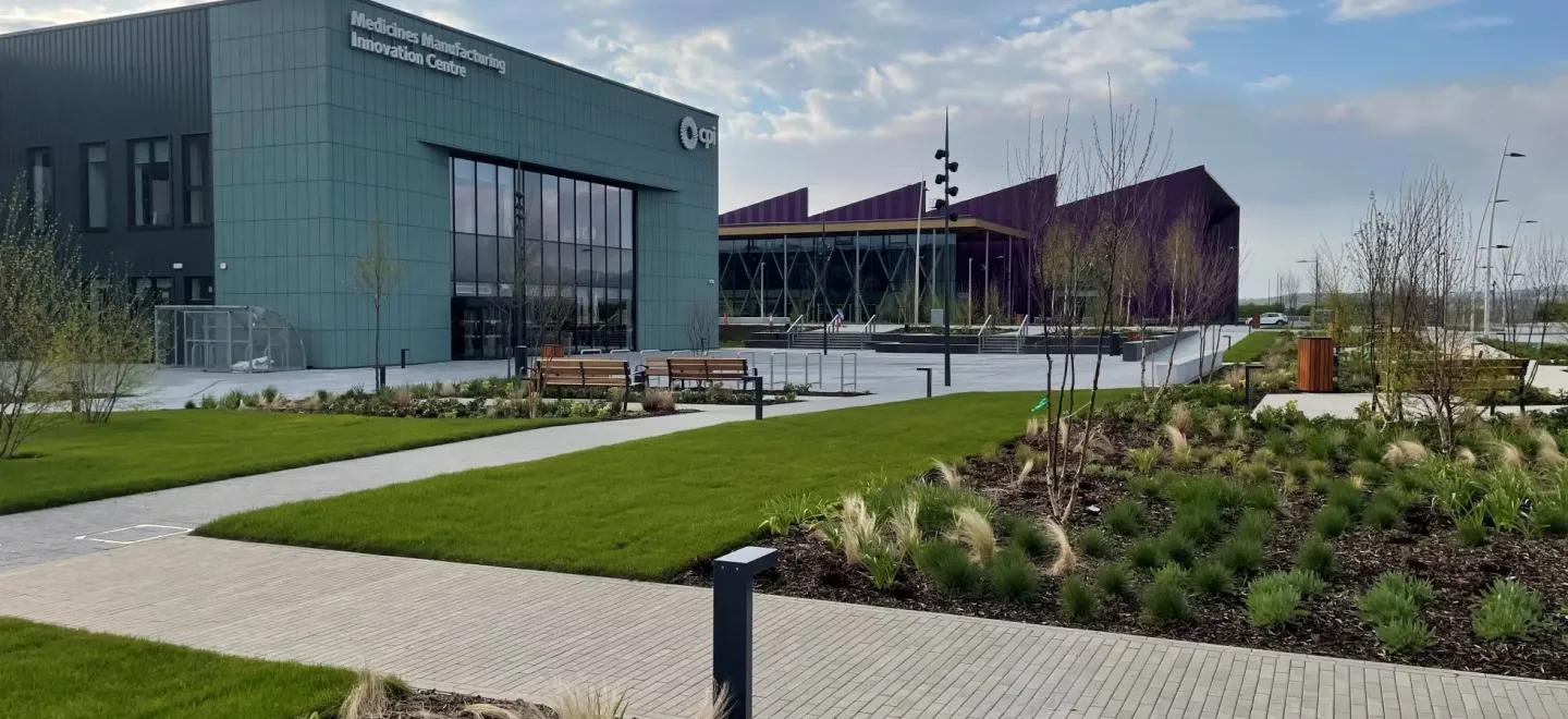 Outside view of the Medicines Manufacturing Innovation Centre, with tidy gardens and a second purple building in the background.
