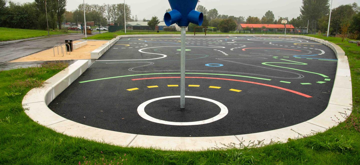 An image of a games area in Ferguslie Park in Paisley. It has a basketball style hoop at the forefront with multi-coloured games space behind.