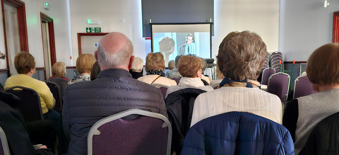 Back of four people's heads as they watch a movie in a community hall.