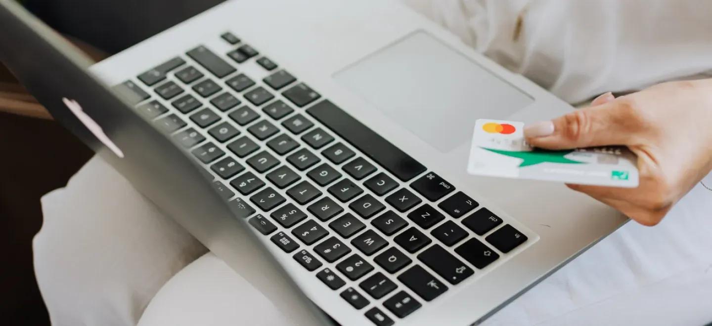 A person sitting with a laptop and holding a bank card.