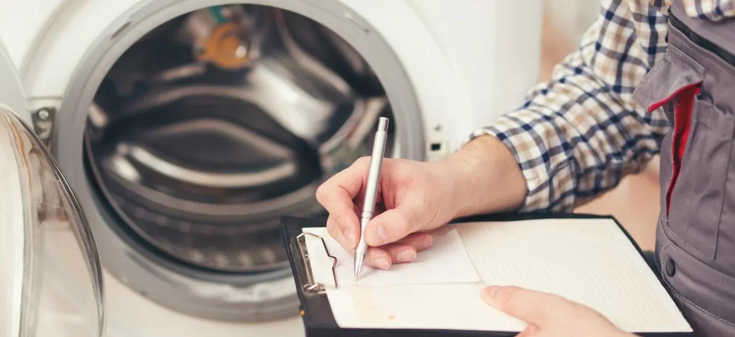 Hand writing on clipboard in front of open laundry appliance