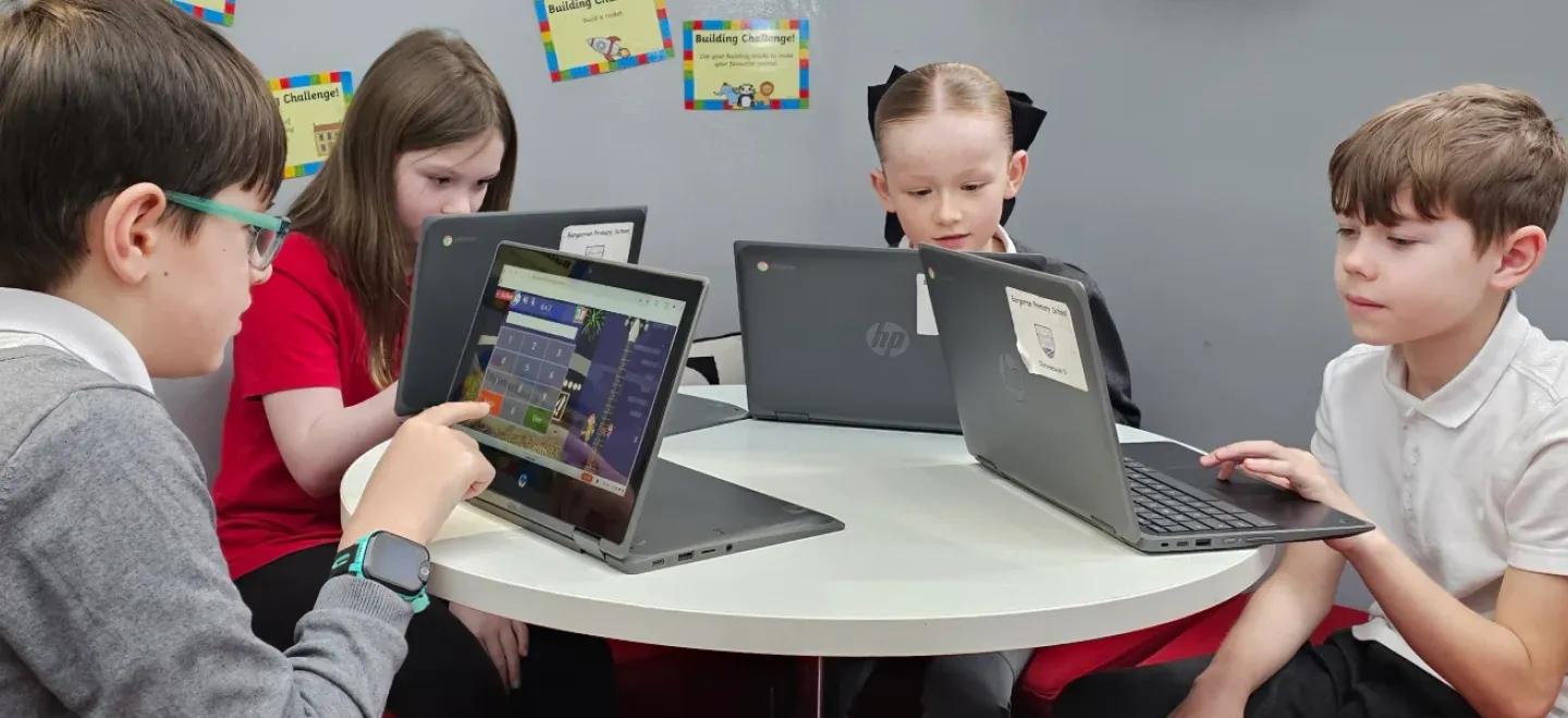 Four primary school pupils sit at a round table using tablet devices.