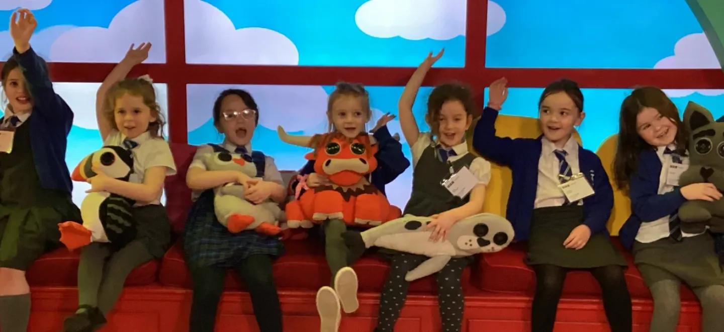 Pupils from the Gaelic unit sit together in a row on a rainbow-coloured window seat.