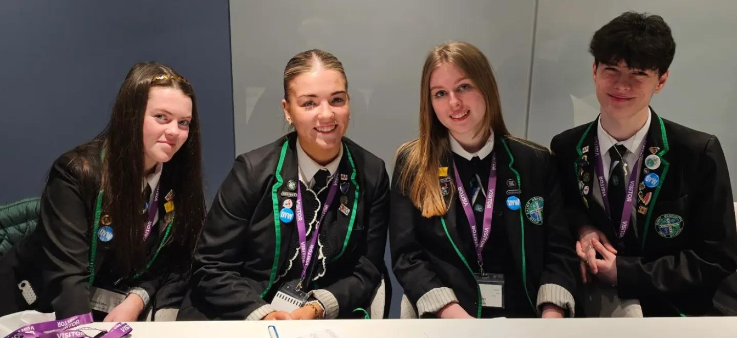 Four senior high school students smile while seated at a desk.