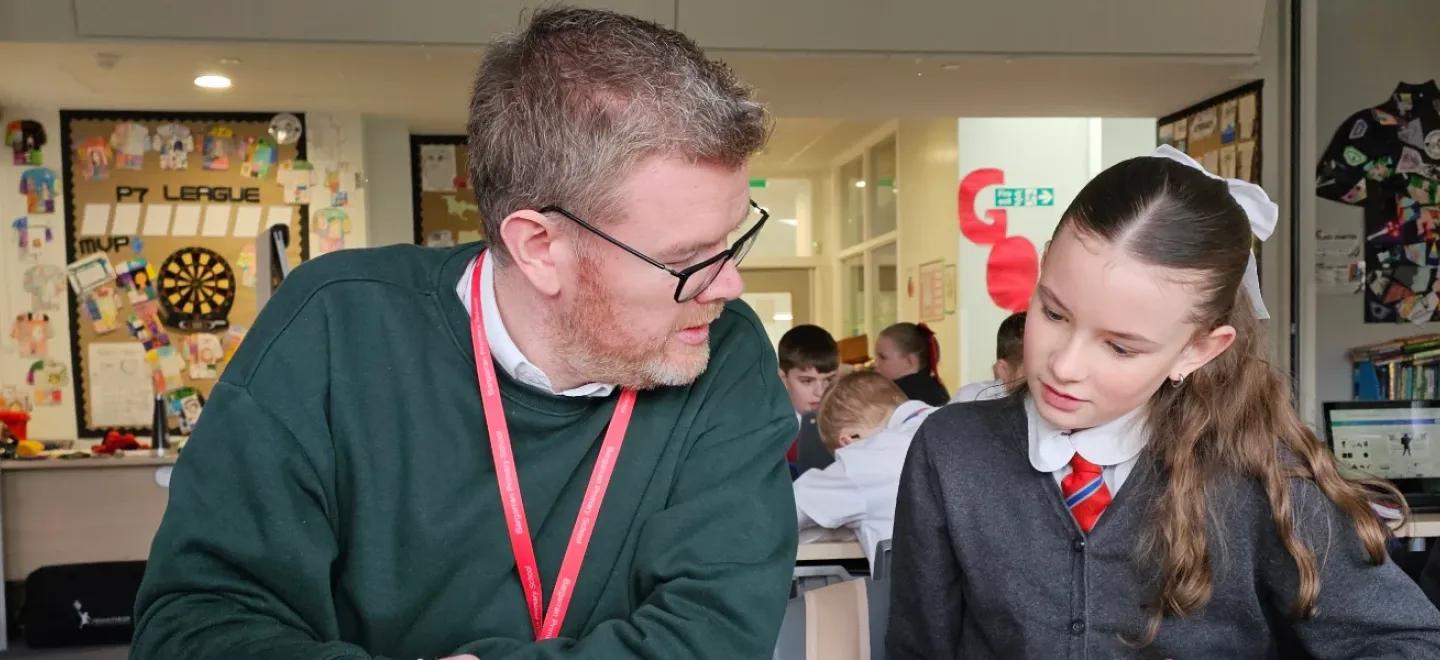 Teacher sits with pupil to discuss solution to coursework lesson.