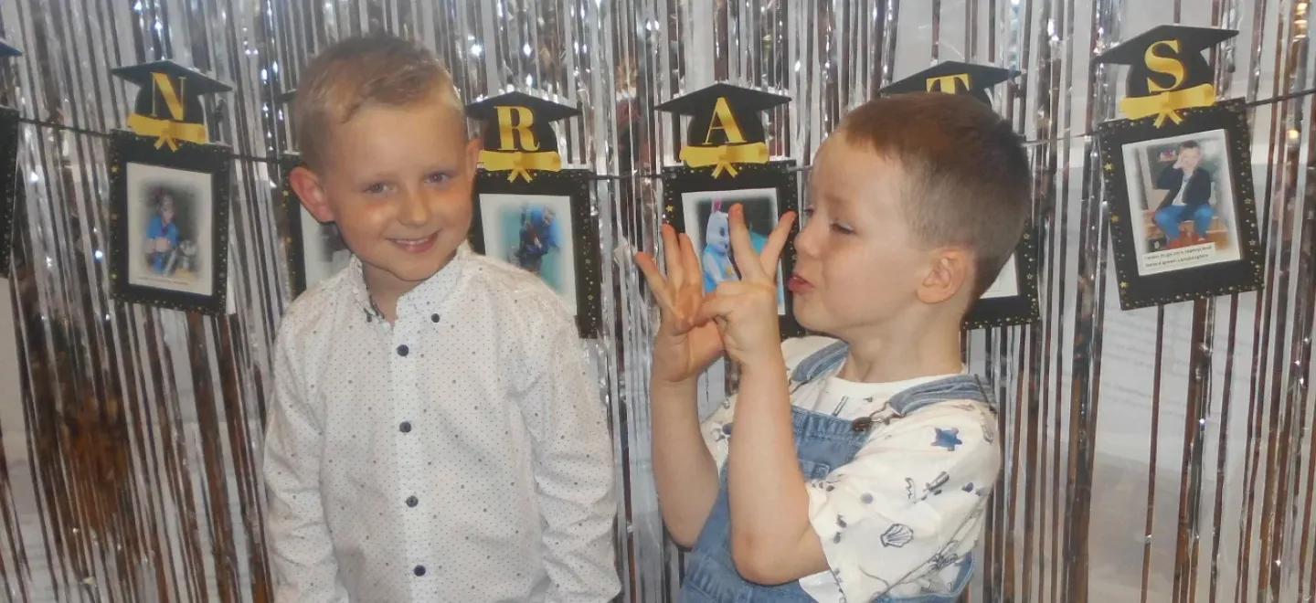 Two children celebrate in front of a graduation banner.