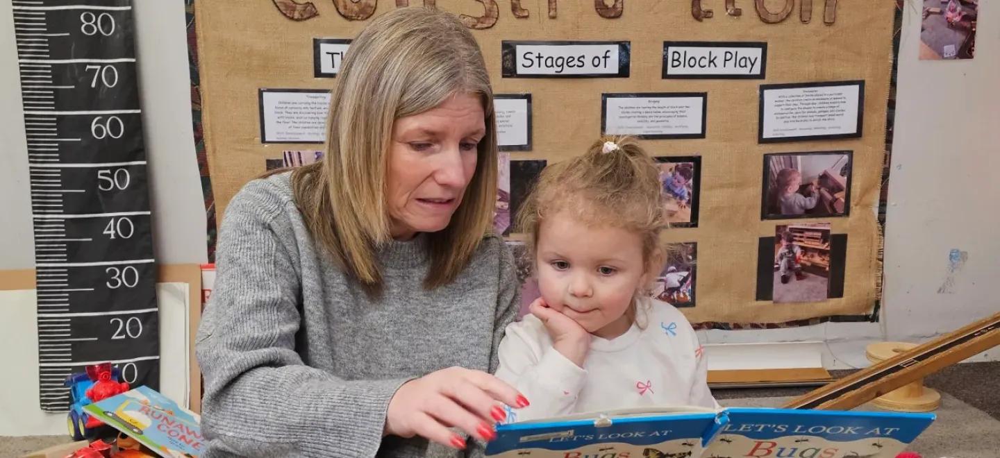 Nursery worker reading a book with a young child.