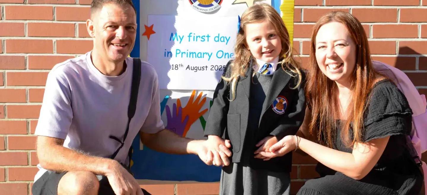 Two parents crouch beside a child who is starting school.