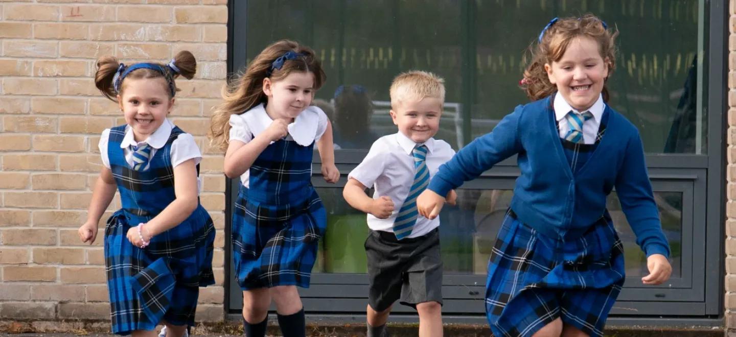 Six primary 1 pupils smile as they run across their playground.
