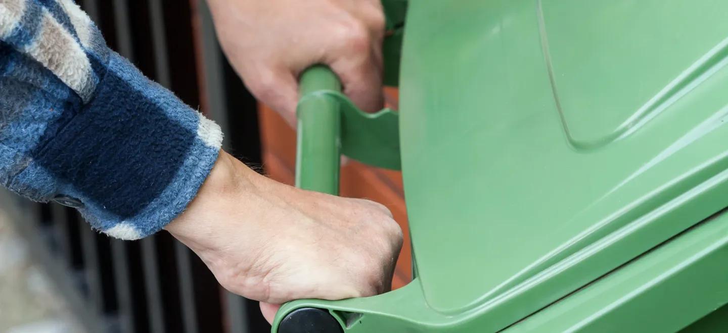 a person pushing a green wheelie bin