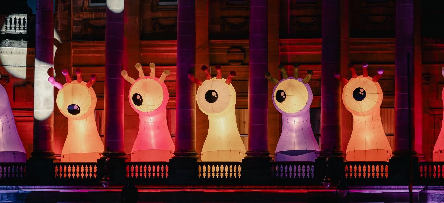 Large illuminated creature sculptures displayed on the balcony of Paisley Town Hall during Paisley Halloween Festival, with colourful lighting projected onto the building.
