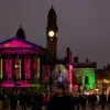 Crowds at Paisley Halloween Parade in front of a lit-up historic building with spooky projections.